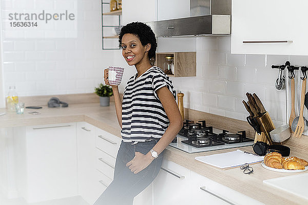 Porträt einer lächelnden jungen Frau  die zu Hause in der Küche einen Becher hält