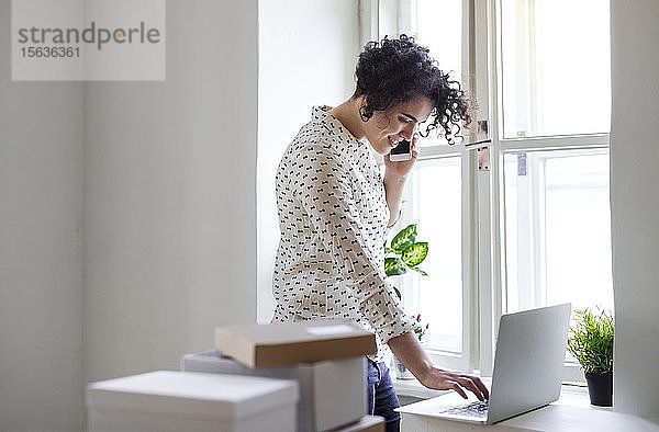 Lächelnde junge Frau am Telefon mit Laptop im Home-Office