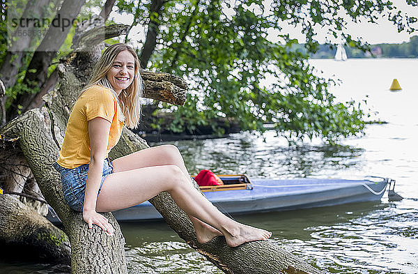 Lächelnde Frau sitzt auf einem Baumstamm am Seeufer