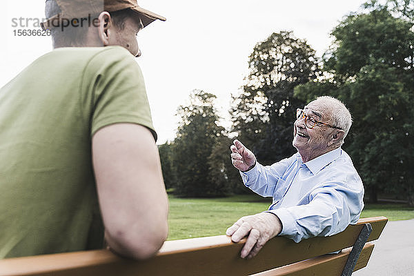 Glücklicher älterer Mann entspannt sich zusammen mit seinem Enkel auf einer Parkbank