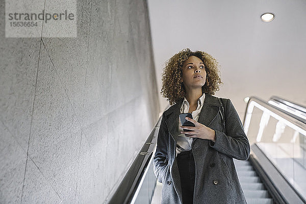 Frau hält Handy auf Rolltreppe