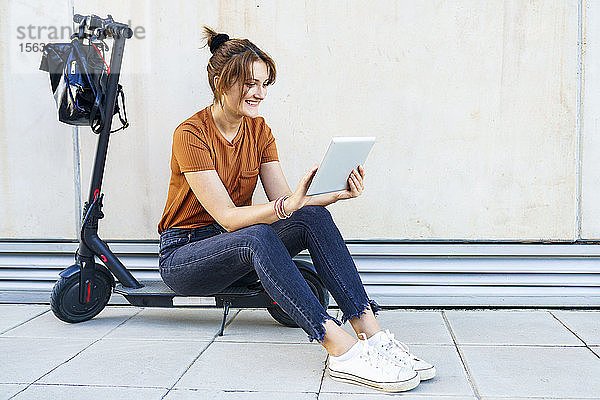Porträt einer lächelnden Frau  die auf einem Elektroroller sitzt und ein digitales Tablet benutzt