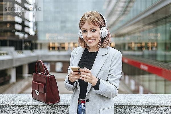 Lächelnde Frau imit Smartphone und Kopfhörern in der Stadt