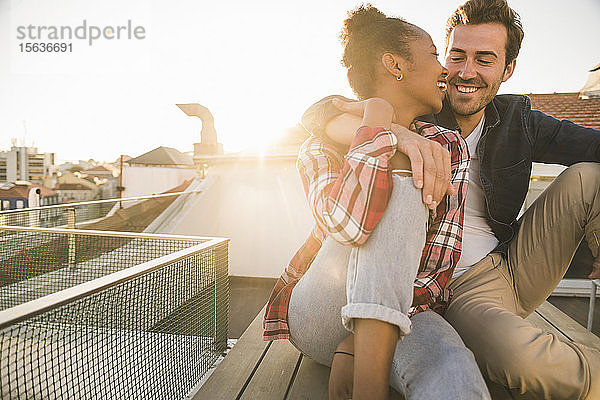 Glückliches  liebevolles junges Paar sitzt bei Sonnenuntergang auf dem Dach