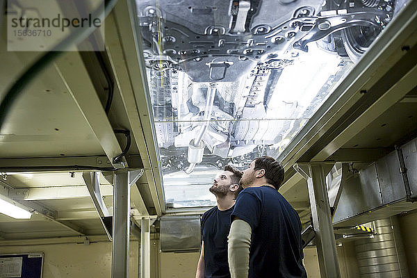Zwei Kollegen in der Fabrik überprüfen Unterboden eines Autos