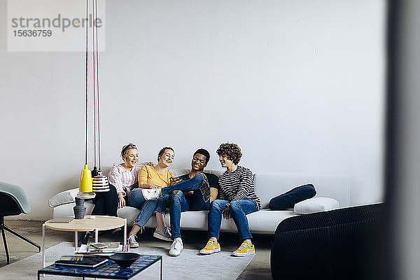 Glückliche junge Leute sitzen zusammen auf der Couch und teilen sich ein Smartphone