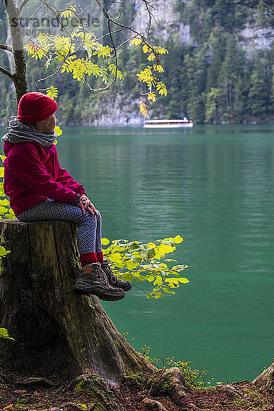 Deutschland  Oberbayern  Mädchen auf Baumstumpf am Keonigssee sitzend