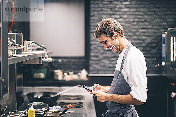 Lächelnder Koch mit Smartphone in der Küche eines Restaurants