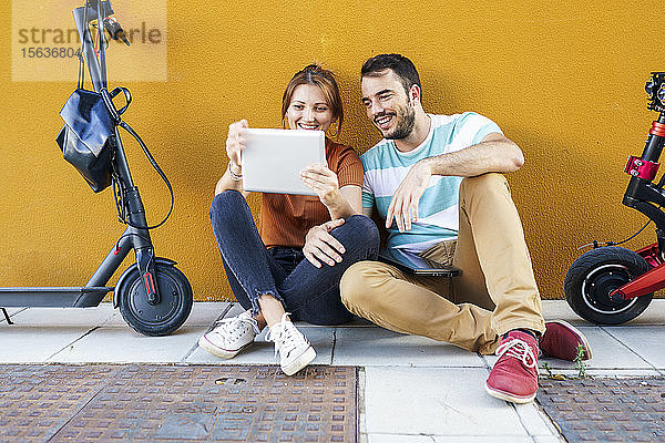 Porträt eines lächelnden Paares mit Elektrorollern mit digitalem Tablet