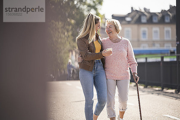Enkelin und ihre Großmutter gehen auf einem Steg und benutzen ein Smartphone