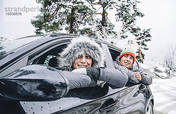 Porträt eines glücklichen jungen Paares  das in einem Auto im Winterwald sitzt und Spaß hat