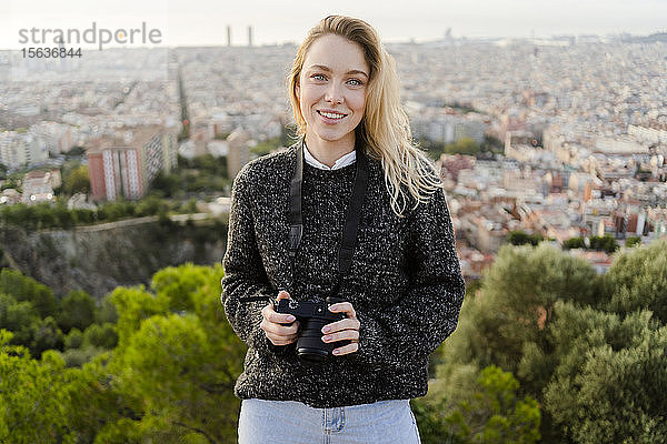Porträt einer lächelnden jungen Frau mit Kamera bei Sonnenaufgang über der Stadt  Barcelona  Spanien