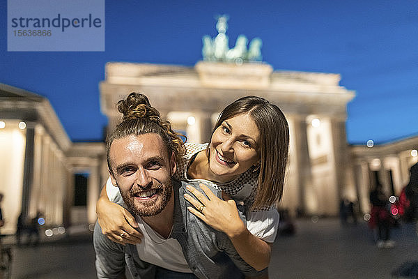 Glückliches Paar am Brandenburger Tor zur blauen Stunde  junger Mann trägt seine Freundin auf dem Rücken  Berlin  Deutschland