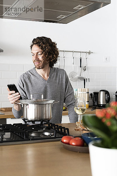 Lächelnder Mann benutzt Handy in der Küche zu Hause