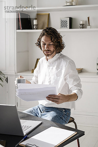 Mann sitzt zu Hause am Tisch und liest Papiere durch