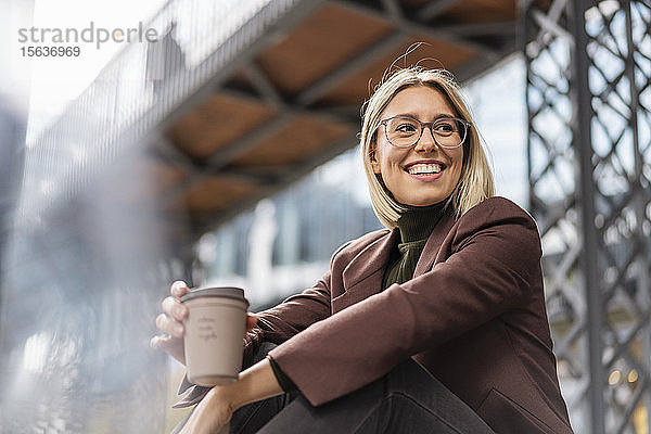 Fröhliche junge Geschäftsfrau mit Kaffee zum Mitnehmen in der Stadt