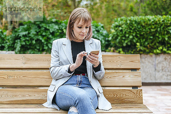 Frau sitzt auf Parkbank und benutzt Mobiltelefon