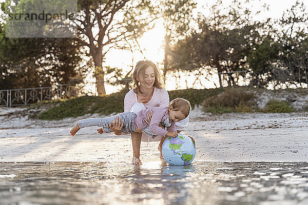 Mutter und kleine Tochter spielen gemeinsam mit Earth Beachball am Meeresufer