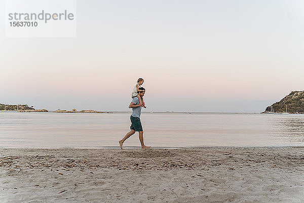 Vater trägt Tochter auf den Schultern am Strand bei Sonnenuntergang