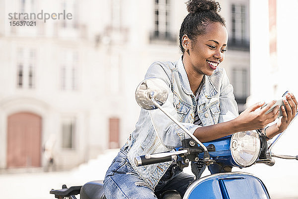 Glückliche junge Frau mit Motorroller und Mobiltelefon in der Stadt  Lissabon  Portugal