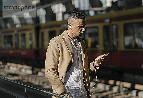 Am Bahnhof stehender Mann mit Smartphone und Kopfhörern  Berlin  Deutschland
