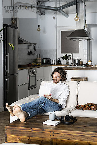 Entspannter Mann sitzt zu Hause auf Couch mit Tablette