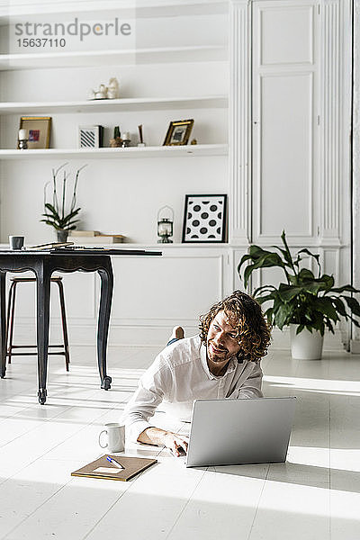 Mann liegt zu Hause mit Laptop auf dem Boden