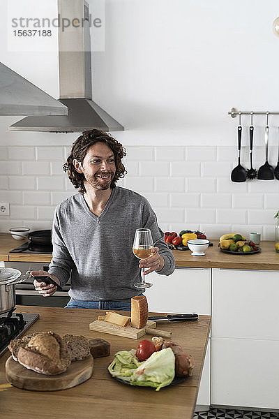 Lächelnder Mann mit Handy in der Küche zu Hause