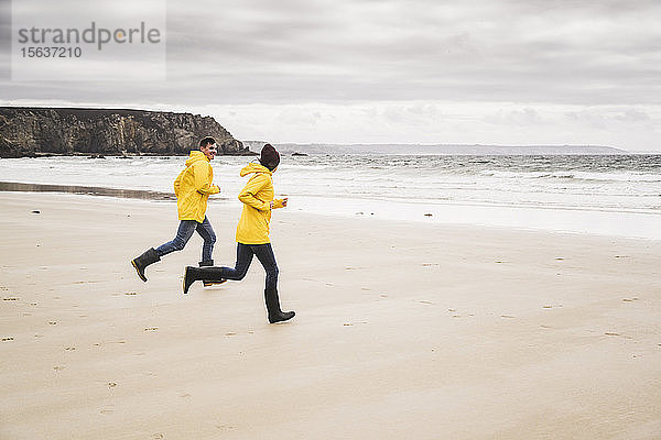 Junge Frau in gelben Regenjacken und beim Laufen am Strand  Bretagne  Frankreich