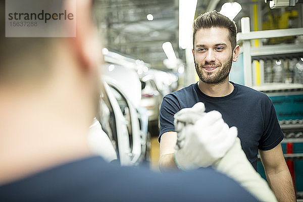 Zwei Kollegen schütteln sich in moderner Autofabrik die Hand