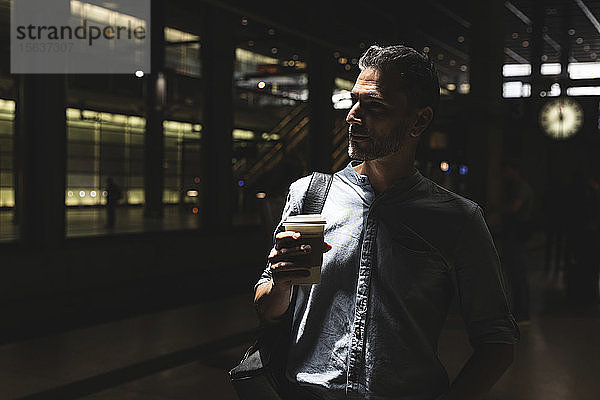 Mann mit Kaffee zum Mitnehmen am Bahnhof im Schatten