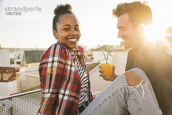 Glückliches junges Paar trinkt bei Sonnenuntergang auf dem Dach