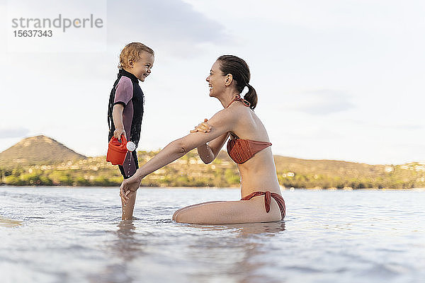 Glückliche Mutter und Tochter spielen mit der Gießkanne im Meer
