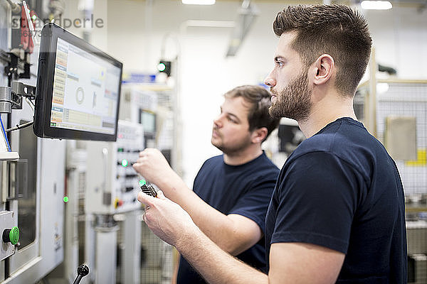 Zwei Männer arbeiten in einer modernen Fabrik und bedienen gemeinsam eine Maschine