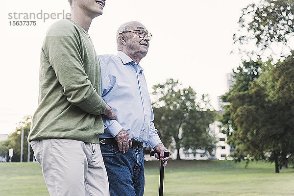 Älterer Mann geht mit Hilfe seines Enkels im Park