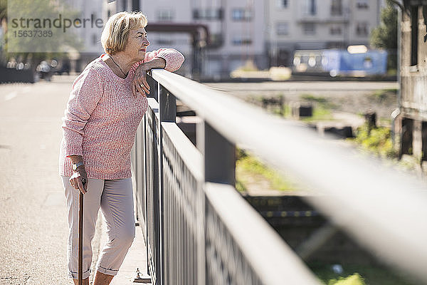 Ältere Frau  die auf einer Fußgängerbrücke geht  mit Gehstock