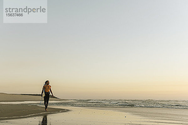 Surfer  die während des Sonnenuntergangs am Strand spazieren