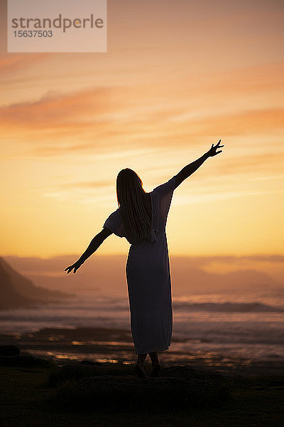 Silhouette einer jungen Frau bei Sonnenaufgang am Strand