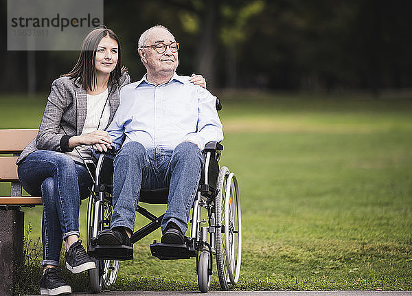 Porträt eines älteren Mannes im Rollstuhl  der sich mit seiner Enkelin in einem Park entspannt