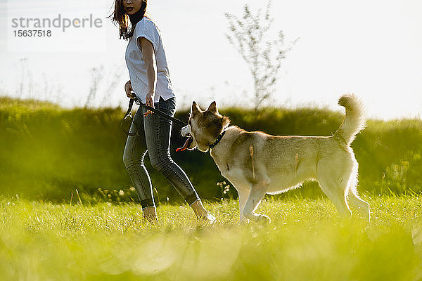 Junge Frau rennt mit ihrem Hund auf einer Wiese