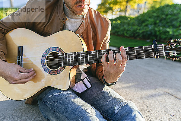 Nahaufnahme eines Gitarre spielenden Mannes in einem Park