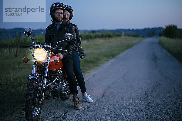 Porträt eines jungen Paares auf einem Oldtimer-Motorrad am Straßenrand
