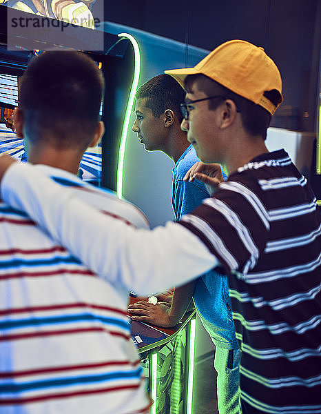 Junge beobachtet jugendliche Freunde beim Spielen mit einem Spielautomaten in einer Spielhalle