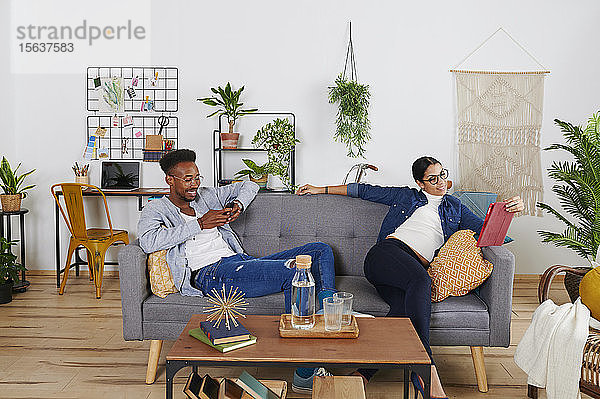Multiethnisches Paar verbringt Zeit zusammen im Wohnzimmer  Frau mit Tablet und Mann mit Smartphone