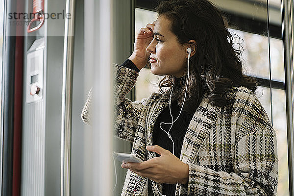 Junge Frau mit Kopfhörern und Smartphone in der U-Bahn