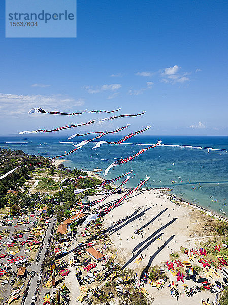 Drohnenansicht von Drachen  die während des Festivals in Bali  Indonesien  gegen den blauen Himmel über den Strand fliegen
