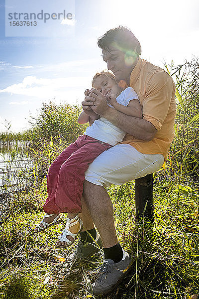 Vater und Tochter sitzen auf einem Holzpfahl an der Küste  Darß  Mecklenburg-Vorpommern  Deutschland