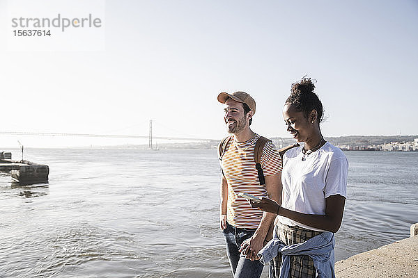 Junges Paar mit Handy auf dem Pier am Wasser  Lissabon  Portugal