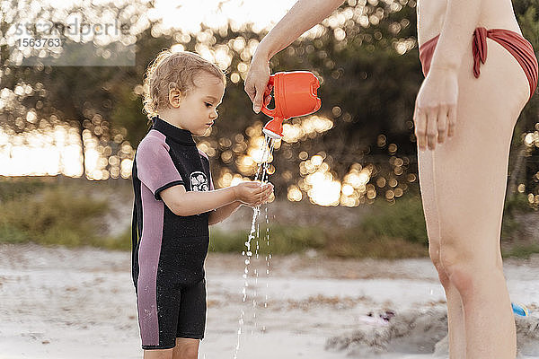 Mutter gießt am Strand Wasser auf die Hände der Tochter