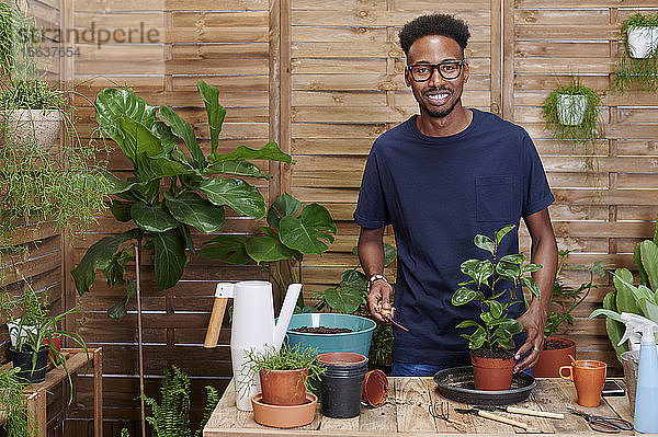 Porträt eines lächelnden jungen Mannes beim Umtopfen einer Pflanze auf seiner Terrasse